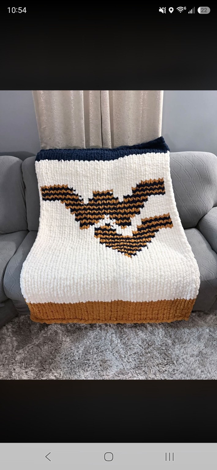 Finished cream chunky-knit blanket with a bold black-and-gold motif and navy edging, displayed on a couch
