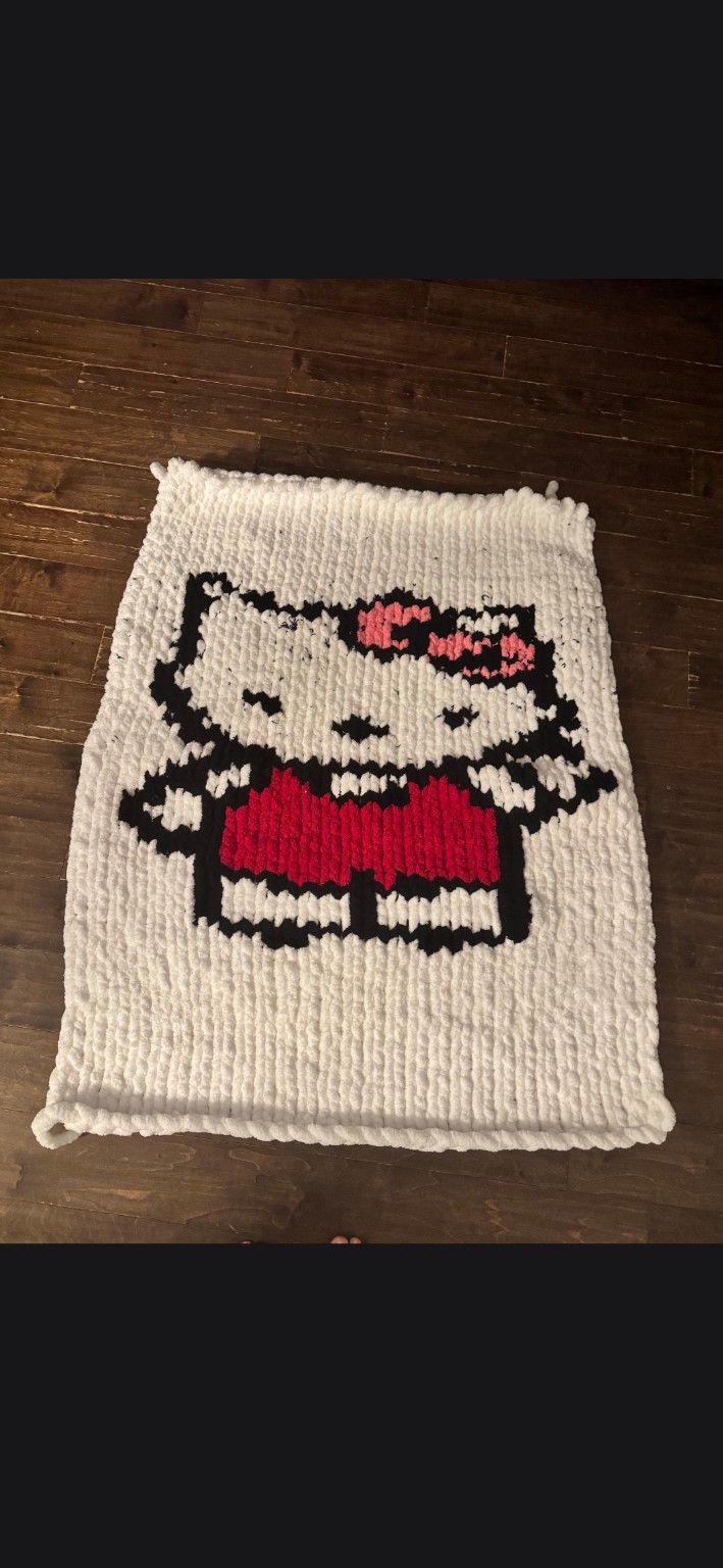 Finished cream chunky-knit blanket featuring a Hello Kitty design, displayed on a wood floor